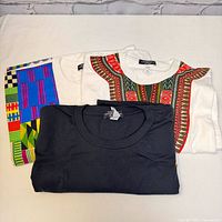 Four African print t-shirts folded to show patterns on collars and sleeves.