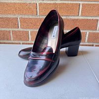 Pair of American Eagle ladies heeled loafers displayed leaning against a brick wall, showing material texture and heel shape.
