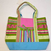 Front view of tote bag showing colorful stripes, pink solid fabric, blue bottom, and striped bow detail.