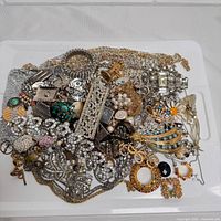 Mixed collection of jewelry pieces arranged loosely to show variety and quantity, including rhinestone brooches, pearl accents, and chains.