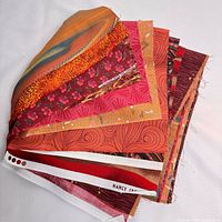 Stack of various fabric fat quarters showing diverse color and pattern range including autumn shades, floral and geometric prints.