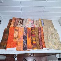 Top view of 20 fabric panels laid flat and unfolded, showing various patterns and colors including browns, oranges, and subtle pastels.