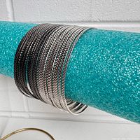 Photo of 20 bangle bracelets with 10 silver color and 10 gunmetal color stacked on a blue foam rod, showing textured surface