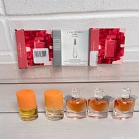 Front view of small bottles including Lancôme La Vie Est Belle with amber liquid, two orange capped sample vials, and boxed perfume samples with red floral designs and one white box labeled L'eau D'Issey Pure