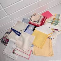 Top down view of the 20 vintage handkerchiefs laid out showing various colors, lace trims, and embroidered floral designs.