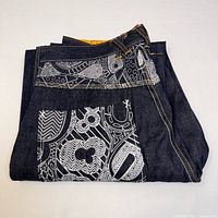 Folded view of dark blue denim jeans displaying the white patterned accent on pocket and waistband area.