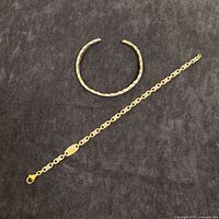 Photo of twisted wrist cuff and titanium link bracelet laid on a dark surface.