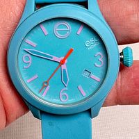 Close-up of watch face showing turquoise dial with pink markers and hands, red second hand, and date window.