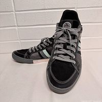 Side angle showing left sneaker with black upper, grey sole, light blue and grey side stripes, laces and toe detail.