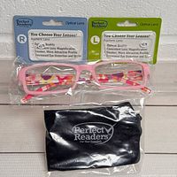 Pink rectangular reading glasses with two sets of packaged +2.75 lenses for right and left eyes, plus black carry pouch in packaging.