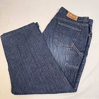 Tommy Hilfiger men's denim jeans folded to display back pocket and leather brand patch on waistband, showing medium-dark blue wash and detailing.