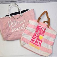 Two pink Victoria's Secret tote bags, one large with white handles and one smaller striped with brown handles and colorful text