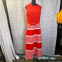 Full view of the vintage 1970s red and white maxi dress on a mannequin, showing sleeveless red bodice and patterned skirt with belt.