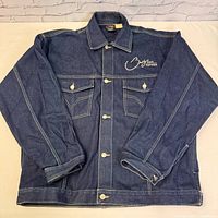 Front view of the dark denim Brooklyn Express jean jacket laid flat showing button front and chest pockets.