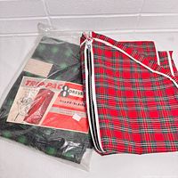 Two vintage plaid garment bags for dresses, one red and black unsealed and one green and black sealed in plastic with original label