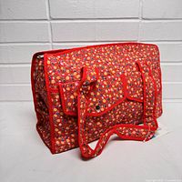 Front and side view showing red floral patterned diaper bag with exterior snap pocket and handles.