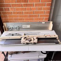 Full view of the Singer Memo-Matic 360K knitting machine with cover and included metal rods laid out on a table.