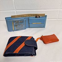 Photo of vintage wallets including blue plastic card holder with gold accents and denim wallet with orange stripes and attached orange pouch