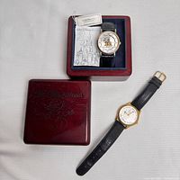 Two Walt Disney World 25th Anniversary watches shown together, one in original wooden box with accompanying booklet, the other loose; both have black leather bands and commemorative dial faces