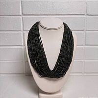 Front view of the women's black beaded multi-strand twist necklace displayed on a white jewelry bust stand, showing the intricate overlapping strands.