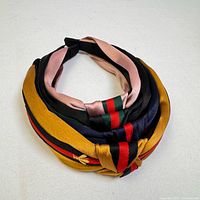 Four women's and girls' cloth and plastic headbands layered together showing their colors and twisted/knot designs in a bundle.