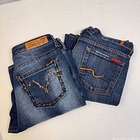 Two pairs of folded women's denim jeans side by side, visible back pockets and brand patches
