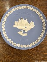 Top view of the blue Wedgwood jasperware Christmas plate showing white relief landmarks, wreath border and swan embellishment.