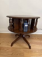 Front view of the revolving book table with a water bottle for scale, showing its round top and lower revolving shelf supported by turned spindles.