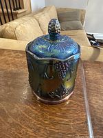 Photo showing the full canister with lid on, highlighting blue iridescent carnival glass and grape and leaf details.
