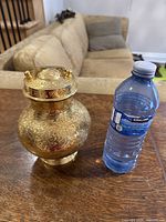 Full view of the vintage brass hand carved water kamandal pot, next to a water bottle for size reference.