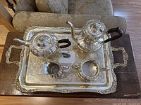 Top view of entire tea set arranged on rectangular ornate silver plated tray showing all five pieces including teapot, coffee pot, creamer, sugar bowl and tray with floral engraving