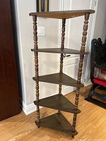 Full view of vintage 5 tier dark wood corner shelf with turned spindle legs and triangular shelves.