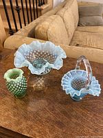 Three vintage glass items displayed on wooden surface: two blue opalescent hobnail glass pieces and one small green hobnail vase.