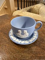 Photo showing the full blue jasperware cup with white classical relief design of a man and woman in profile.