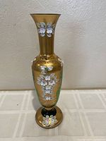 Front view of tall Bohemian green glass vase decorated with 24K gold paint and hand-painted white floral designs.