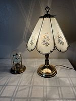 Table lamp with floral paneled shade and Haller glass dome clock on left, lit for display