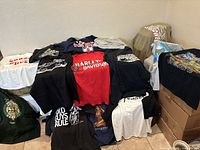 Overview of lot with multiple t-shirts showcasing various motorcycle and vintage themed designs, including Harley-Davidson and skeleton graphic.