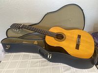 Hohner HG 14 classical guitar lying inside an open padded soft case on table. Full guitar body and neck visible with wood finish and strings.