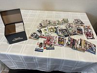 Photo showing a large spread of assorted football sports cards on a table alongside a black football collectors box.