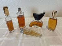 Five perfume and fragrance bottles arranged on a table showing varying bottle designs and amber liquid inside.
