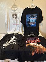Four rock concert t-shirts on hangers, front view showing graphics for Jim Morrison, Bob Dylan, Neil Young, Lynyrd Skynyrd