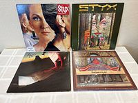 Four Styx vinyl LP records with original jackets: Grand Illusion, Cornerstone, Paradise Theater, and Pieces of Eight promo. All arranged on a white surface.