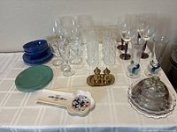Overview of kitchen bundle items arranged on table including blue plates and bowls, assorted glassware, vintage butter dish, salt & pepper set, and ceramic spoon rest.
