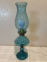 Front view of the blue glass electrified hurricane lamp showing the tall chimney with diamond pattern and rounded body with pedestal base. Cord is visible, lamp is unplugged and unlit.