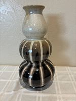 Front view of the tall, three-tiered ceramic vase showing beige top and striped dark brown middle and bottom tiers.