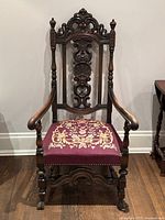 Front view of the antique armchair showing intricate carved backrest and needlepoint seat.