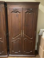 Front view of the antique style pine armoire showing the double carved doors and metal handles.