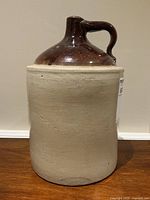 Front view of the antique whiskey jug crock showing the full height and handle with two-tone glaze.