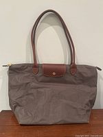 Front view of taupe nylon Longchamp Le Pliage tote with brown leather flap and handles, showing slight wrinkling and texture