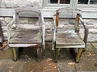 Front view of the pair of weathered outdoor wooden armchairs showing the natural aging and wear on the seat and arms.